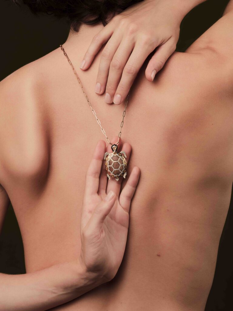 A photography of the nude back of a model wearing an elegant necklace with a turtle pendant made of diamonds. The picture was taken for Aloisia, a jewelry brand whose visual identity and art direction was curated by Osmo.