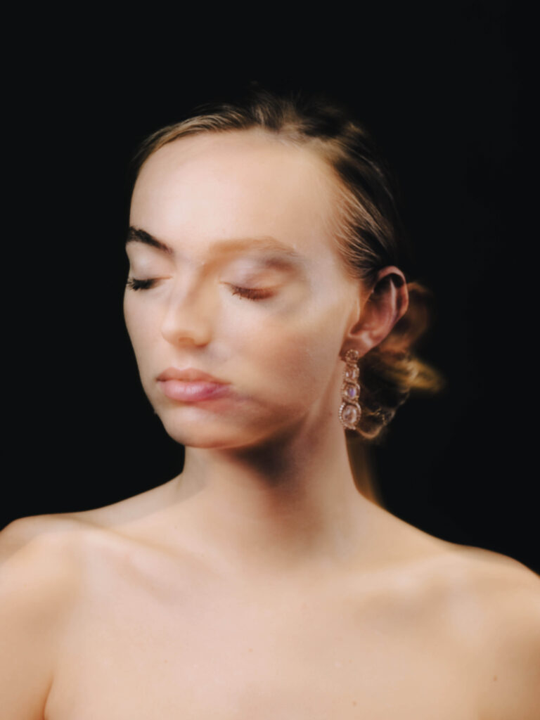 A photograph of a model on a black background wearing elegant pendant earrings crafted by Aloisia, a jewelry brand whose visual identity and art direction was curated by Osmo.