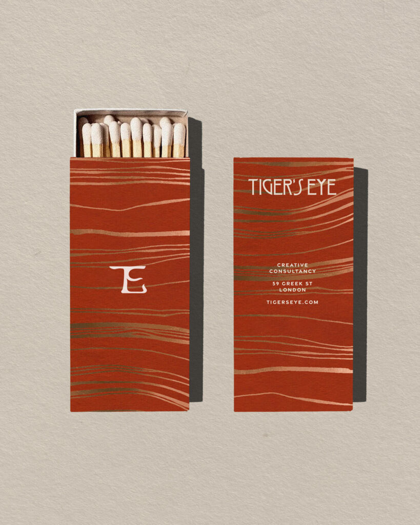 Two matchboxes, with Tiger's Eye symbol on the front and the logo on the back with the contacts. The boxes have a luxury feel with a red pattern and gold foil details.